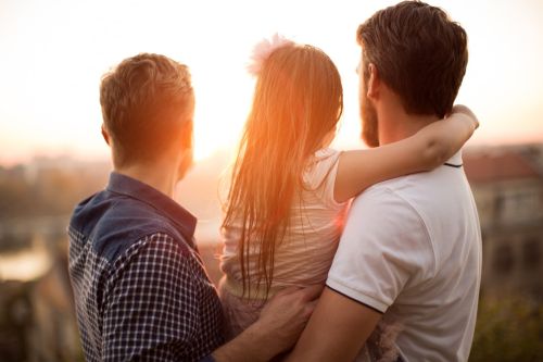 Young gay parents with their daughter having fun in park. Parents holding girl in arms. Enjoying in beautiful sunset. Caucasian ethnicity. Visual concept for a legal blog on issues same-sex couples face during divorce.